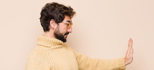 young cool man looking serious, stern, displeased and angry showing open palm making stop gesture...