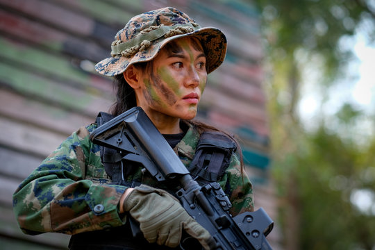 Beautiful Asian woman soldier hold the gun and stand with resting position to prepare for fight in battle field.