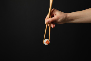 Fototapeta premium Female hand with chopsticks hold sushi roll on black background. Japanese food