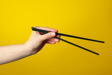 Female hand with chopsticks on yellow background, close up