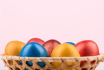 Basket with multi-colored Easter eggs on a pink background.