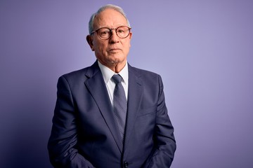 Grey haired senior business man wearing glasses and elegant suit and tie over purple background looking sleepy and tired, exhausted for fatigue and hangover, lazy eyes in the morning.
