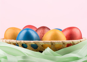 Basket with multi-colored Easter eggs and a green ribbon on a pink background.