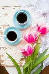 coffee, croissants and three beautiful pink tulips on old white table