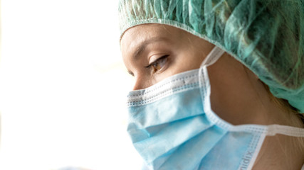 One woman, worried female doctor in protective suit, looking through the hospital window.
