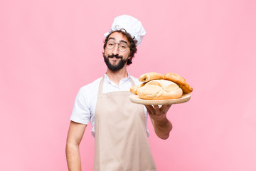 young crazy baker man holding bread against pink wall