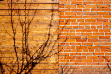 A shadow of a tree falls on a wooden and brick wall of a house.