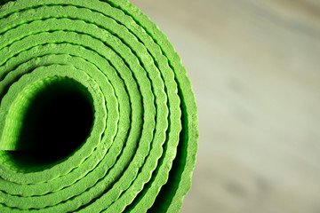 Fototapeta na wymiar The yoga mat of green color lies on the floor. Healthy lifestyle. Light background in blur.