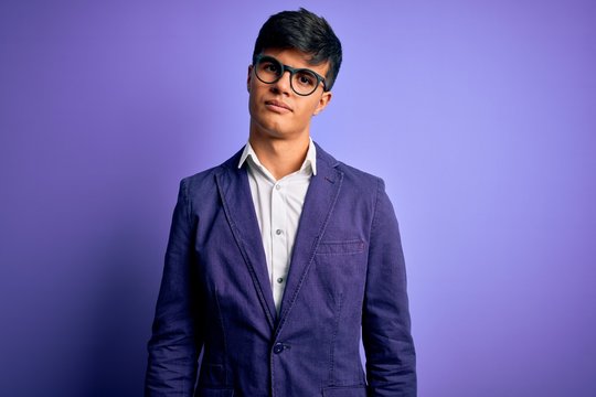 Young handsome business man wearing jacket and glasses over isolated purple background Relaxed with serious expression on face. Simple and natural looking at the camera.
