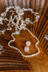 Beautiful set of pearls woman accessories: necklace, hairpins, earrings. Expensive and delicate bridal jewelry lying on unique wooden table with carving. White gems jewellery