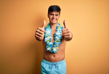 Young handsome tourist man on vacation wearing swimwear and hawaiian lei flowers approving doing...