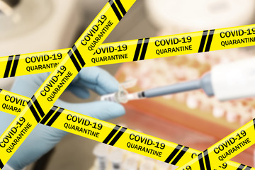 Coronavirus warning tapes against hand of scientist in blue glove making sampling of material from...