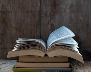 Un libro abierto colocado en tres libros, sobre un fondo de madera rústica, celebración del día del libro.