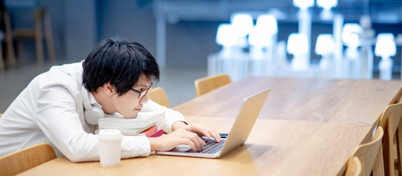 Young Asian man university student with glasses and headphones using laptop computer for online learning course at home. E-learning on internet during quarantine. Study from anywhere concept