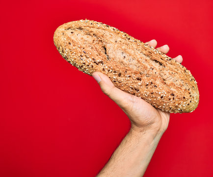 Beautiful hand of man holding wholemeal integral bread with cereals over isolated red background