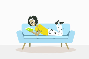 Cute young woman is lying on a comfortable sofa with a book in the room.