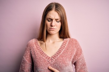 Fototapeta premium Young beautiful redhead woman wearing casual sweater over isolated pink background with hand on stomach because indigestion, painful illness feeling unwell. Ache concept.