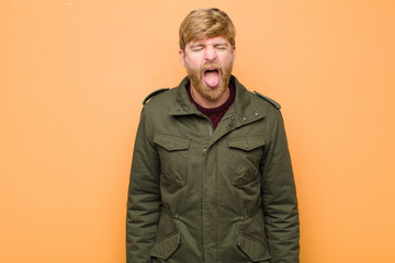 young blonde man with cheerful, carefree, rebellious attitude, joking and sticking tongue out,...