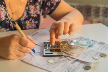 an elderly woman considers payments for utility bills; on a calculator, she considers payment for an apartment with money in Russian rubles; banknotes of 2000,100 rubles and Russian coins