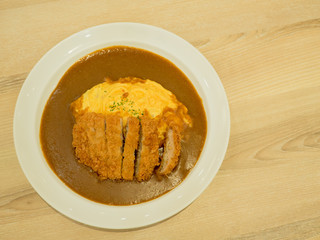 Curry Rice with Crispy Pork Cutlet and Omelette on wooden table.