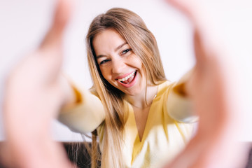 Cheerful young woman holding camera and making selfie while standing against white background