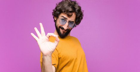 young crazy cool man feeling happy, relaxed and satisfied, showing approval with okay gesture, smiling against flat wall - obrazy, fototapety, plakaty