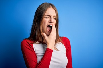 Young beautiful redhead woman wearing casual t-shirt over isolated blue background bored yawning tired covering mouth with hand. Restless and sleepiness.