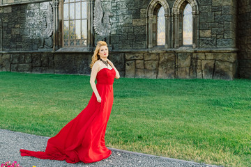 A woman in a red dress stands on a background of a medieval castle