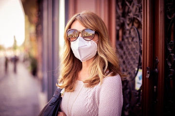 Close-up shot of middle aged woman standing on the street and wearing respirator mask for health protection while rapidly spreading coronavirus outbreak in the city.