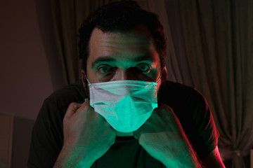 Portrait of a man in a medical mask. Isolation of the house in quarantine. The emotions of fear and...