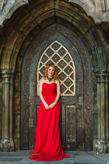 A woman in a red dress stands on a background of a medieval castle