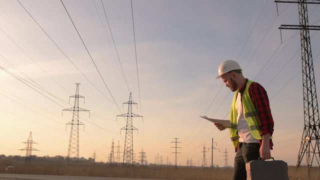  engineer in a white helmet checks blueprint on the background of power lines