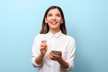 closeup young cheerful businesswoman with beautiful healthy smile holding pen making new ideas notes and interestedly looking up against blue background