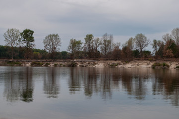 Blue river slow flowing across the green meadow and yellow sand with reflections of  trees in the water.  Fall