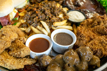 Close up of unhealthy food - steak, fried chicken, hamburger, ham, sauce, black pepper, french fries and meat ball on a big bowl.