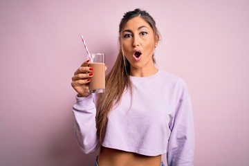 Young beautiful fitness woman drinking protein chocolate milkshake before gym scared in shock with...