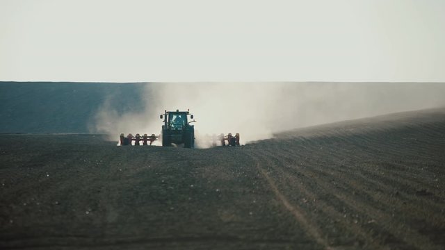 Green tractor with a seeder goes across the field, carried out by spring seeding