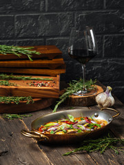 Side view on a delicious dish of home-made seabass fillet with mushrooms and potatoes in a saucepan in a pan on a wooden table, vertical format
