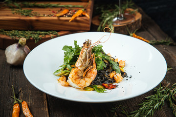 Side view on italian cuisine dish shrimp and arugula spaghetti with ink cuttlefish on the white plate on the dark wooden table, horizontal