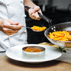 Chef hand cooking pasta penne with mozzarella cheeze in a white plate, square format