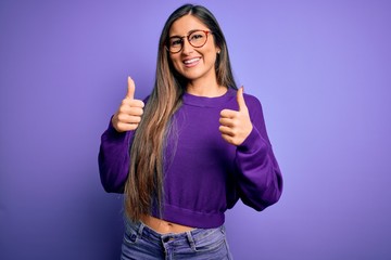 Young beautiful smart woman wearing glasses over purple isolated background success sign doing positive gesture with hand, thumbs up smiling and happy. Cheerful expression and winner gesture.