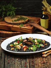 Side view on italian cuisine dish black risotto with seafood on the white plate on the dark wooden table, horizontal format