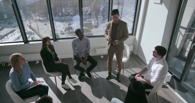 Top view confident young businessman in formal clothes teaches lessons of mistakes and life hacks for businessmen for mixed race audience In a bright and spacious conference room