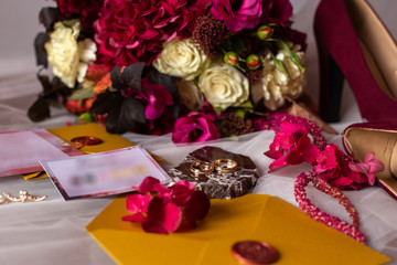 wedding accessories: a bride’s bouquet of roses, peonies and hydrangeas, wedding rings on a stone, a ring and earrings with diamonds, women's shoes, invitation and yellow envelopes with a red wax seal