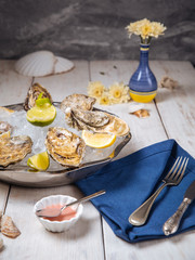 Side view on a metallic bowl with fresh appetizing oysters with ice and lemon on the white table with cutlery, vertical format