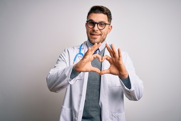 Young doctor man with blue eyes wearing medical coat and stethoscope over isolated background smiling in love doing heart symbol shape with hands. Romantic concept.