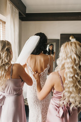 Back view of a bride in a wedding dress and bridesmaids helping her to dress