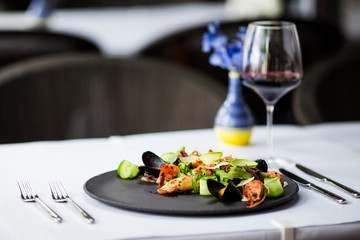 Side view on the white restaurant table served with italian cuisine dish seafood salad with a glass of red wine, horizontal format