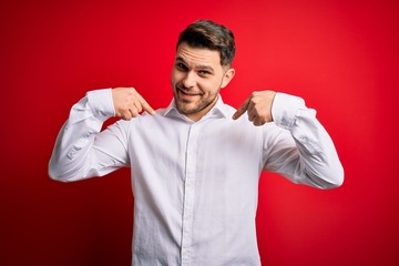 Young business man with blue eyes wearing elegant shirt standing over red isolated background looking confident with smile on face, pointing oneself with fingers proud and happy.