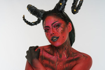 young pretty girl doing body painting characterized by demon with big black horns and red and black...
